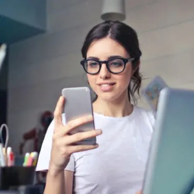 Donna con occhiali sorride guardando lo smartphone